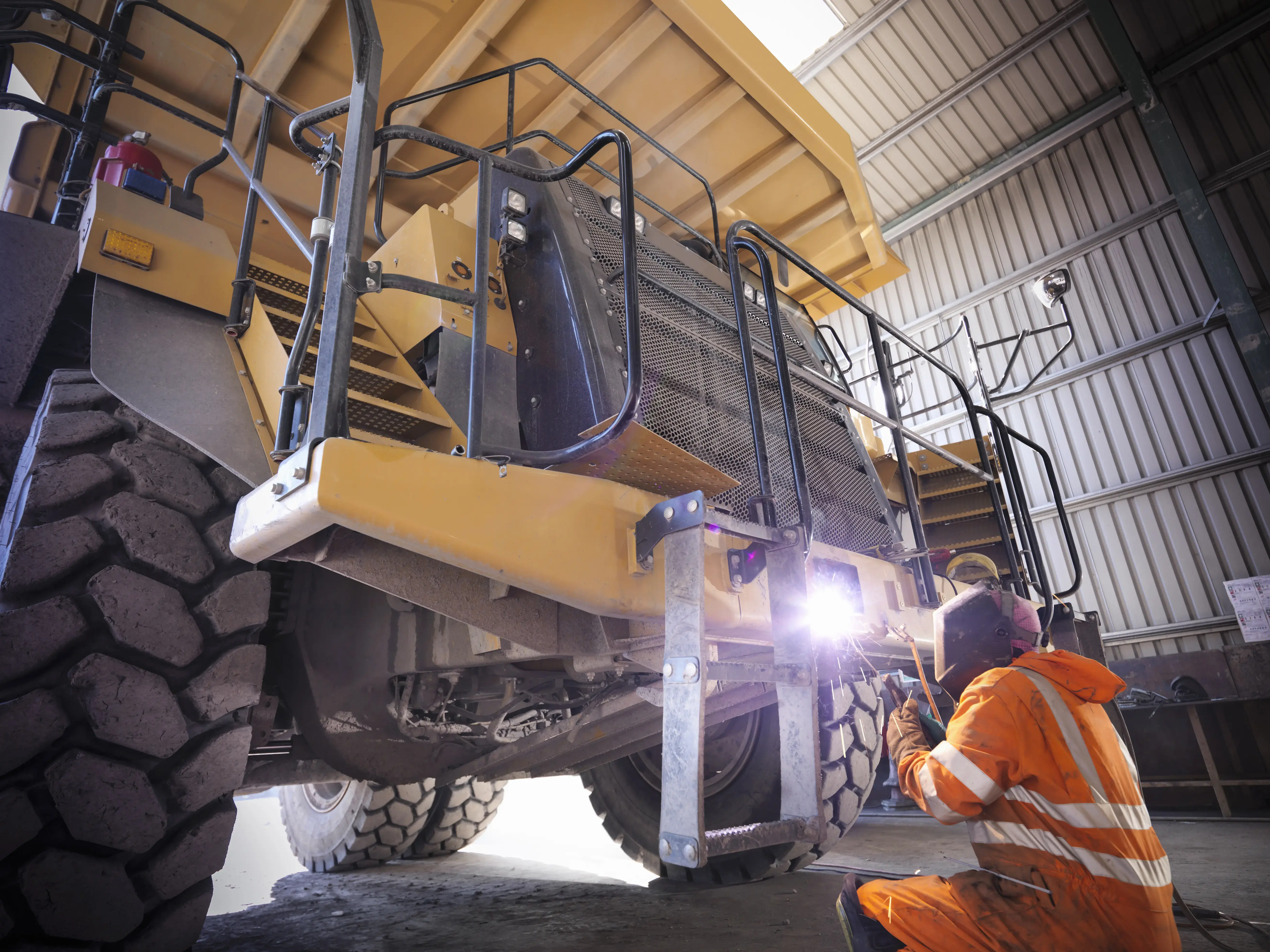 Miner welding dumper truck in opencast coalmine